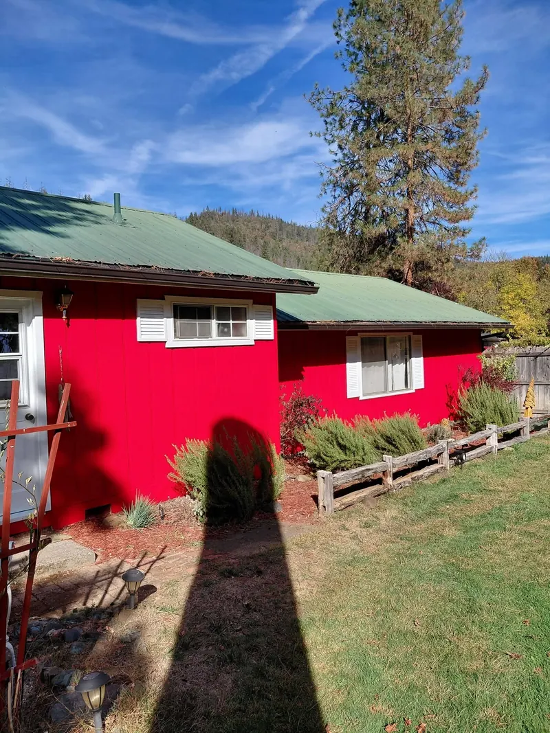 Two sections of the red home under green metal roofs, with white-shuttered windows and a split-rail border along a sunny lawn.